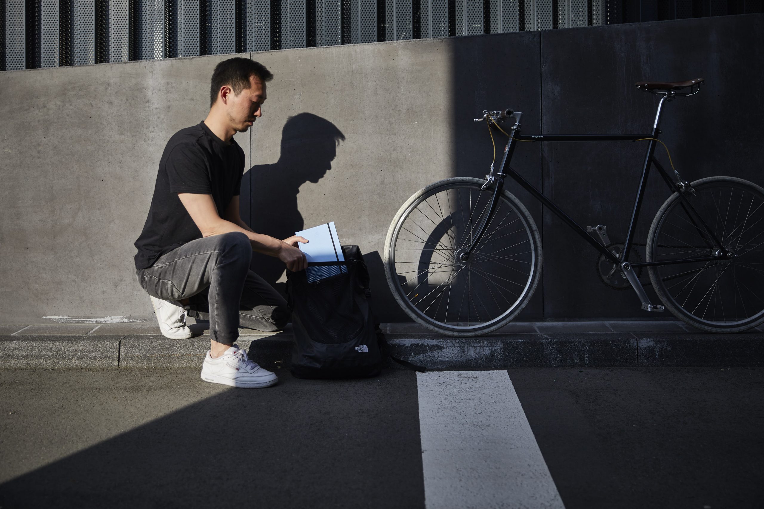 Mann steckt blaues Buch in den Rucksack, neben ihm sein Fahrrad